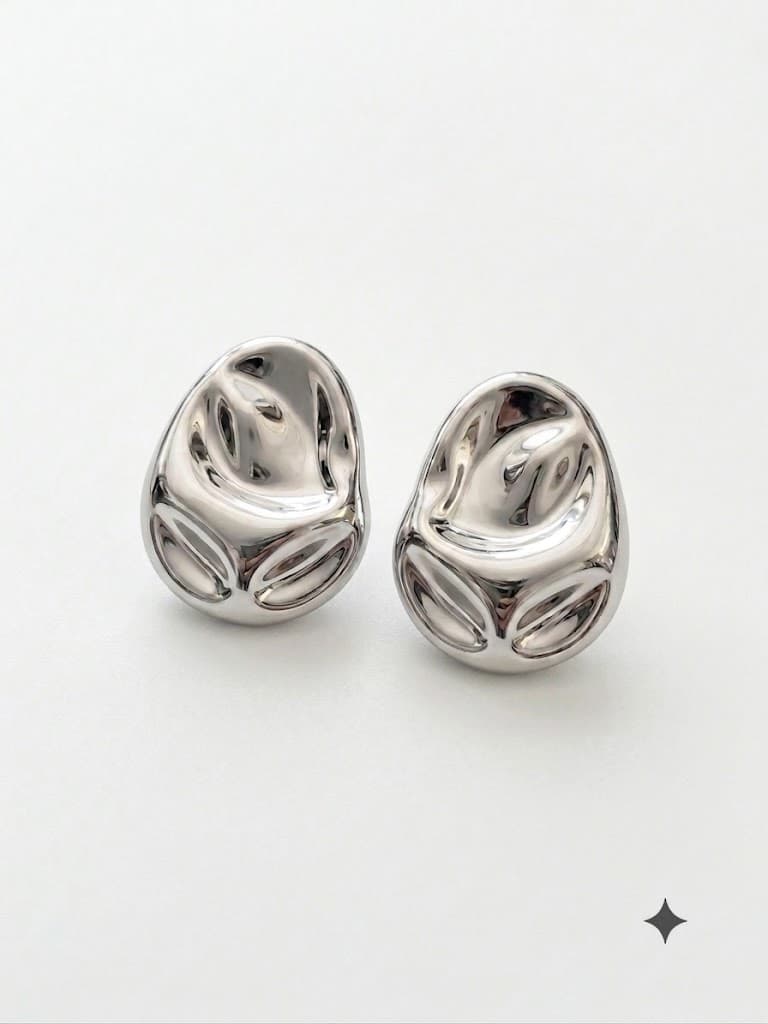 Pair of domed teardrop silver stud earrings with a mirror finish and carved oval facets along the lower edge, on a pale grey backdrop.