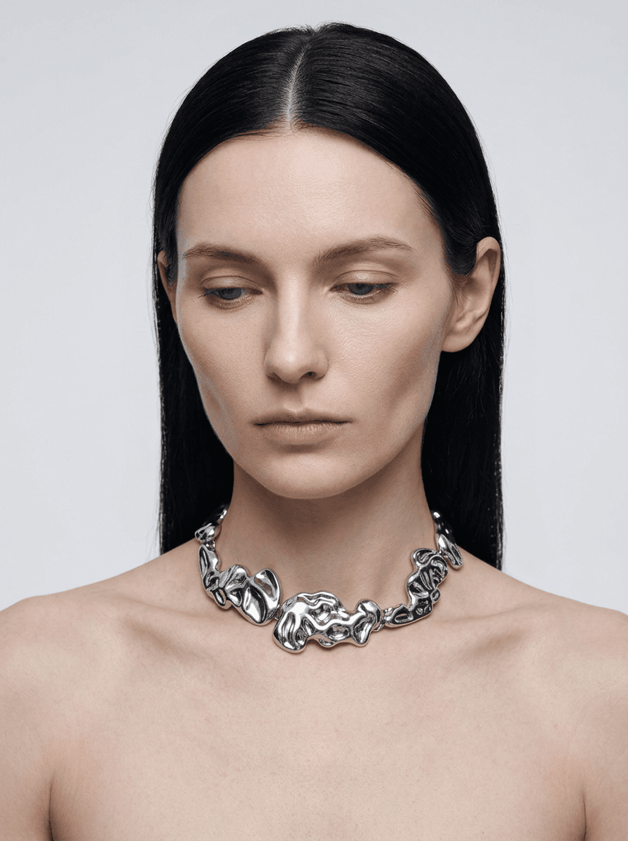 Sculptural chrome jewellery worn on the skin against a pale backdrop.