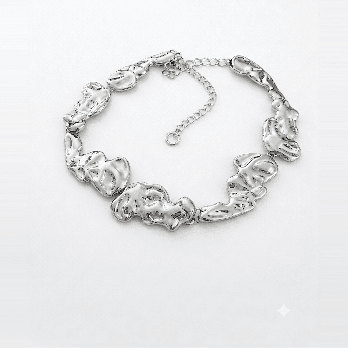 Silver collar necklace of large crushed molten plates linked together, closed with an extender chain, on a pale grey backdrop.